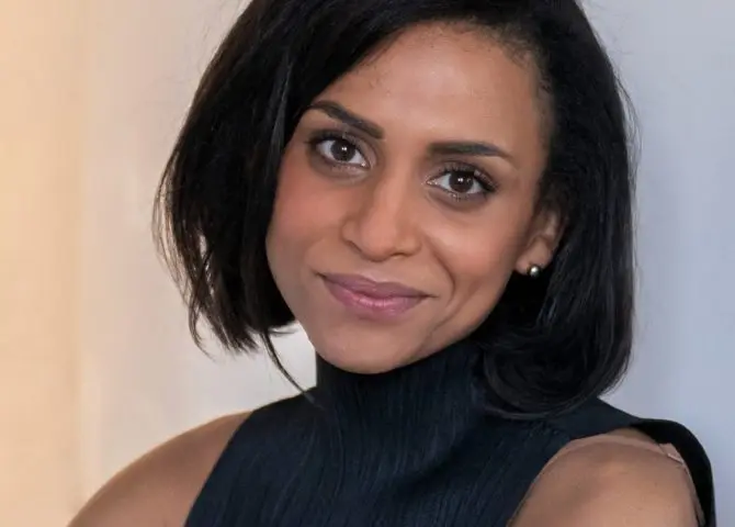 An image of the Black writer Rachel Long. She has chin length black hair and is wearing a sleeveless black pleated black top with a high neck.
